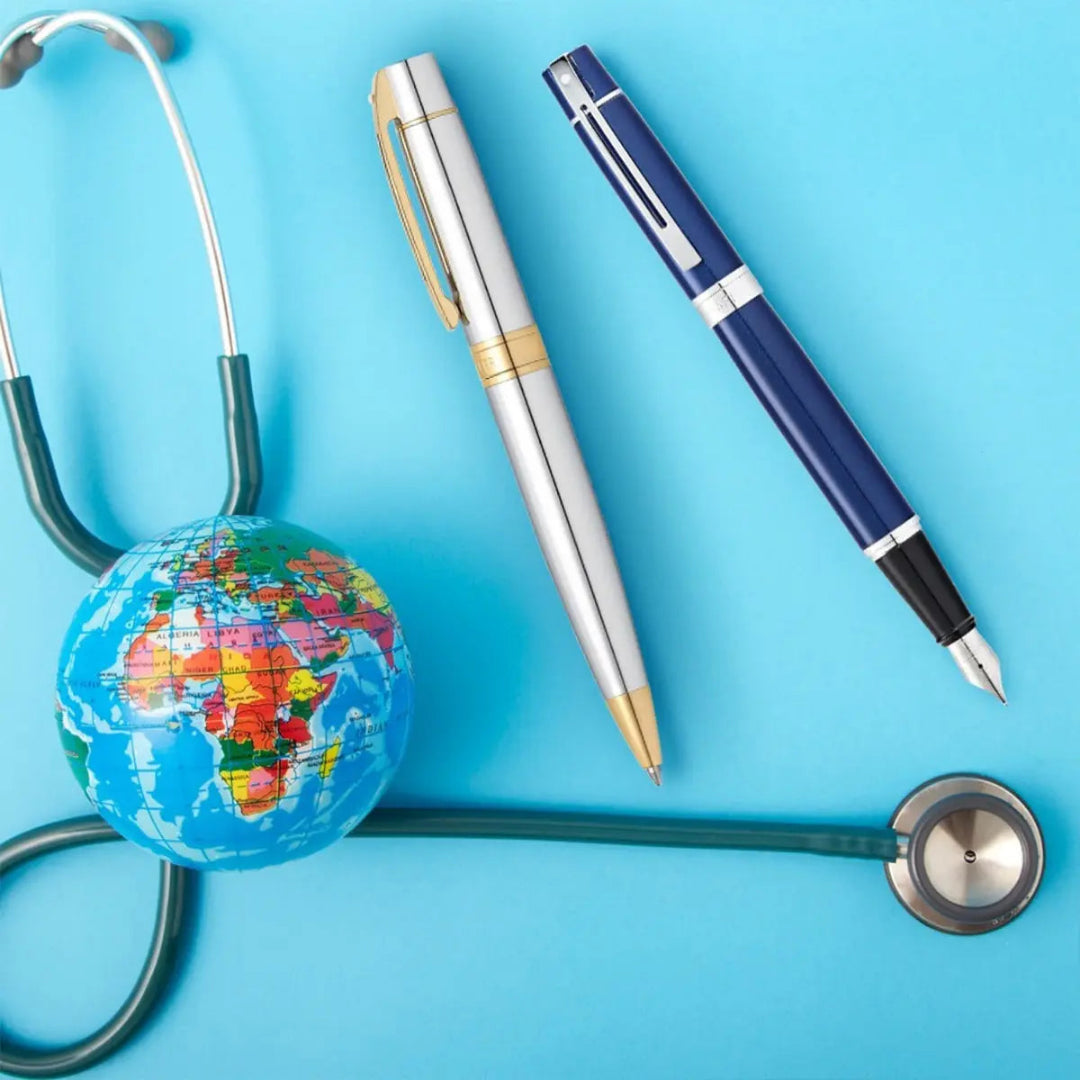 Sheaffer 300  Bright Chrome Ballpoint Pen With Gold Trims beside sheaffer blue fountain pen, stethoscope and globe