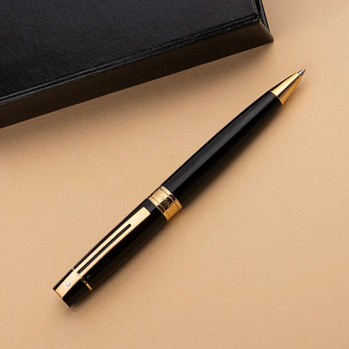 Sheaffer 300 Glossy Black Ballpoint Pen with Gold Trims beside leather notebook